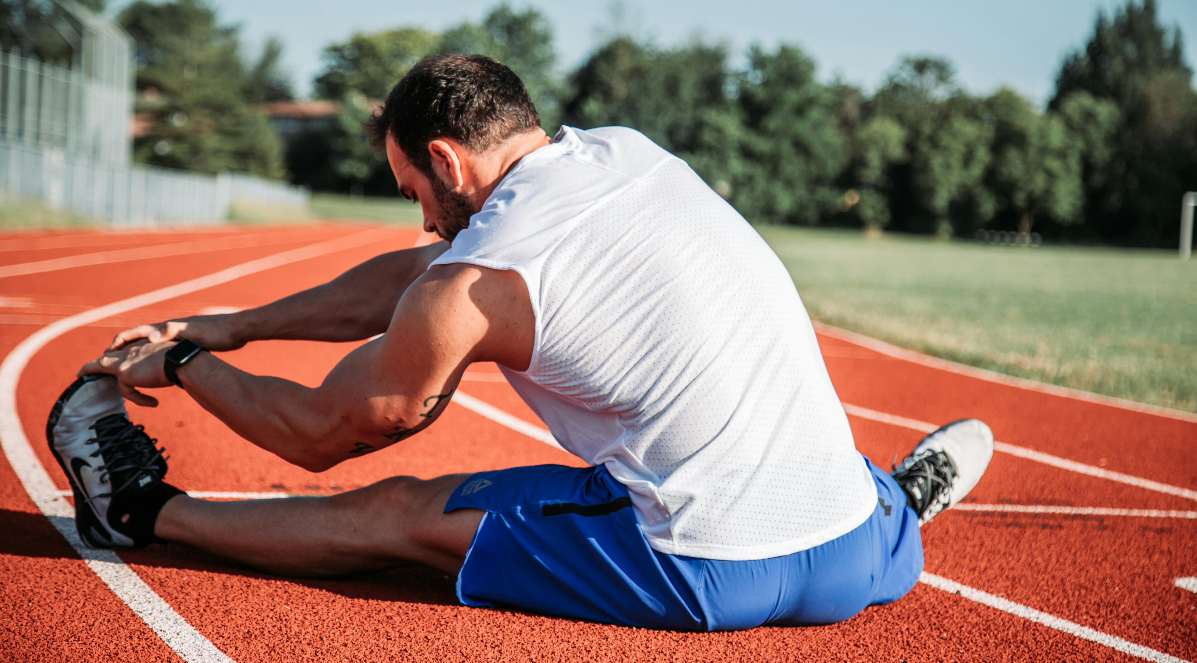 Flexibility & mobility coaching A person doing a seated hurdlers stretch on a track field, increasing his flexibility.